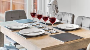 Una mesa de comedor dispuesta con cuatro copas de vino, platos, cubiertos y posavasos negros.