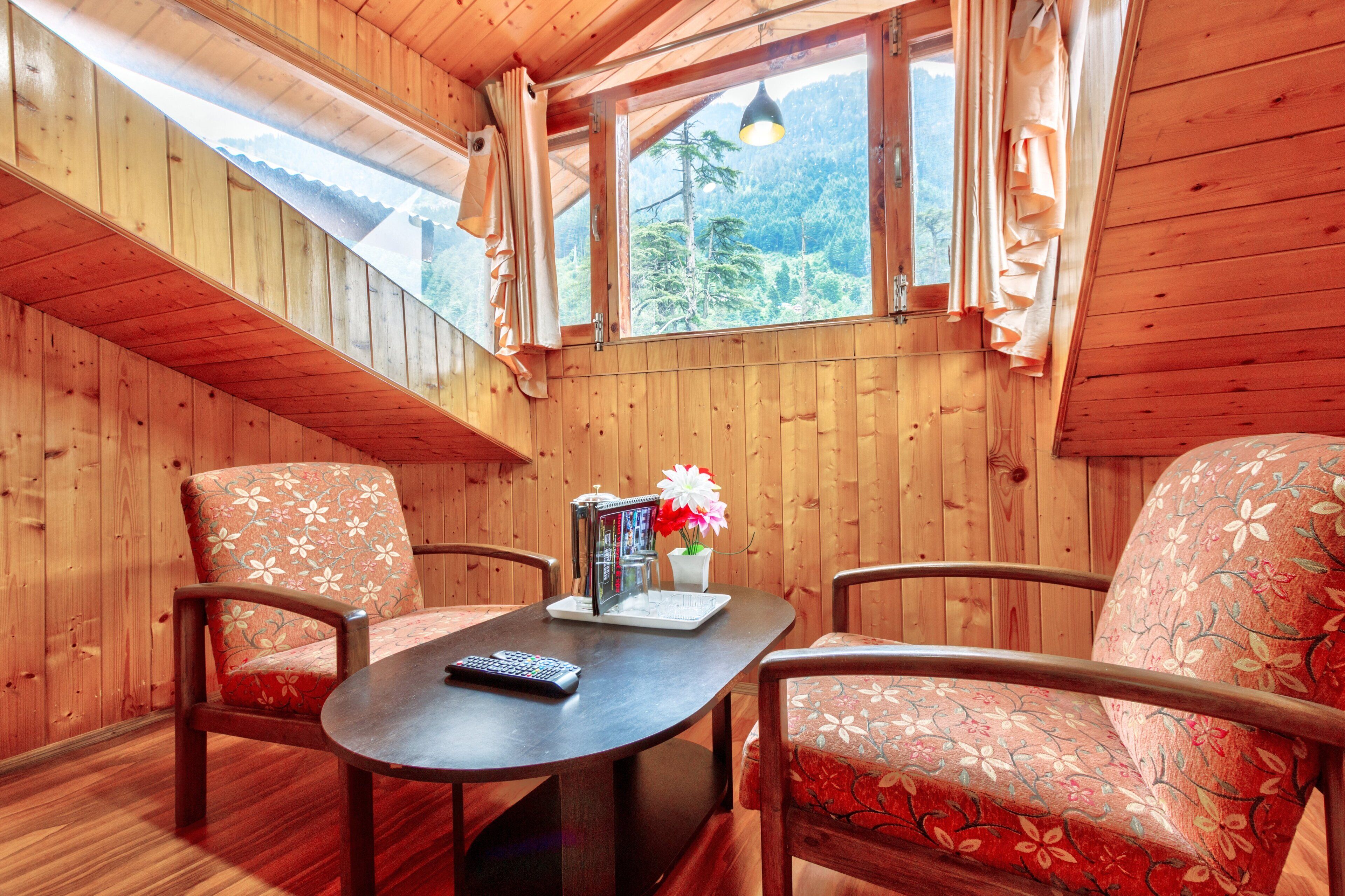 A cozy wooden cabin with a dining table, two floral-patterned chairs, a remote control, and a vase with flowers.
