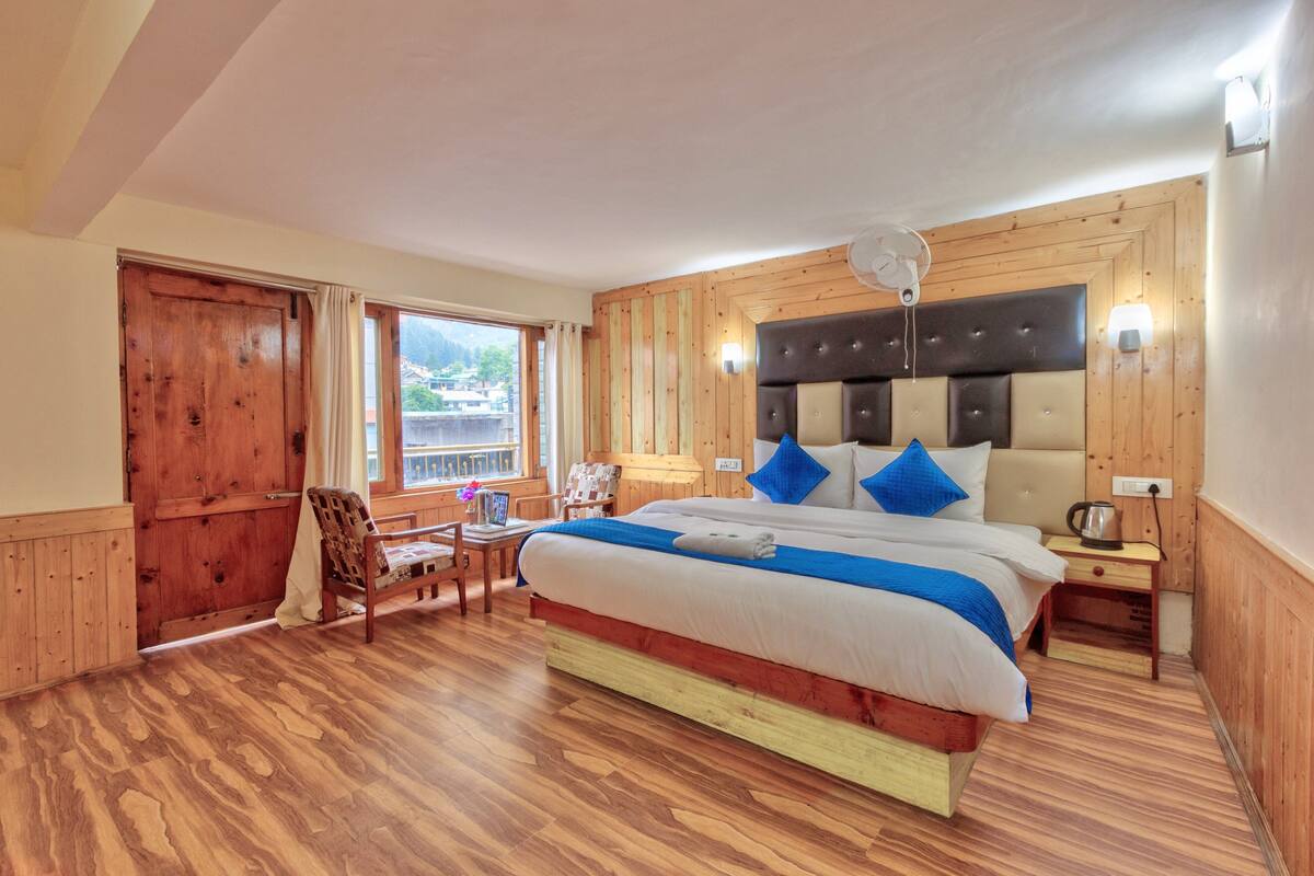 Une chambre aux murs lambrés, avec un lit, une chaise, une table et une fenêtre donnant sur un beau paysage.