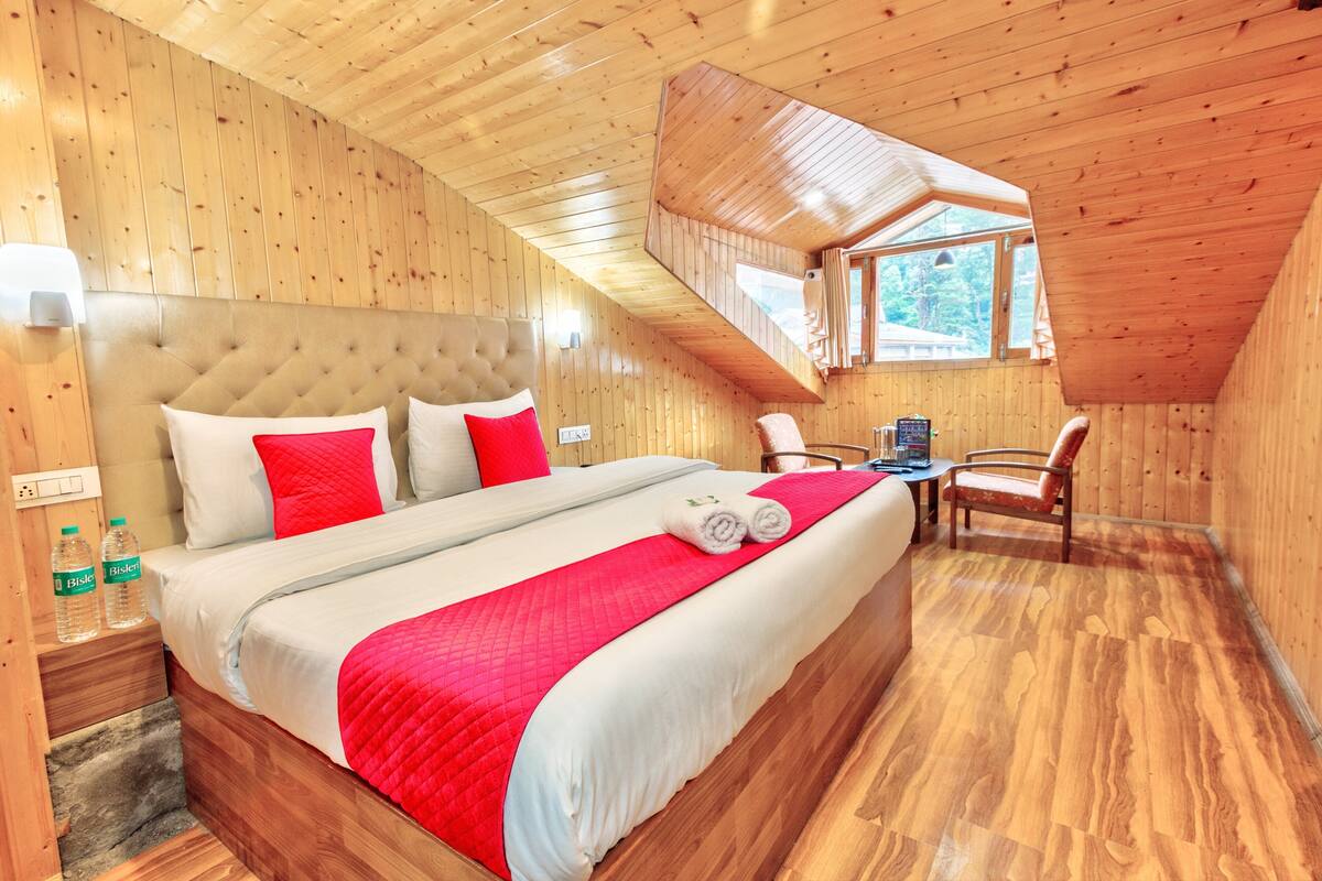 Une chambre aux murs lambrissés, avec un grand lit, une literie rouge et blanche, une petite table et une chaise.