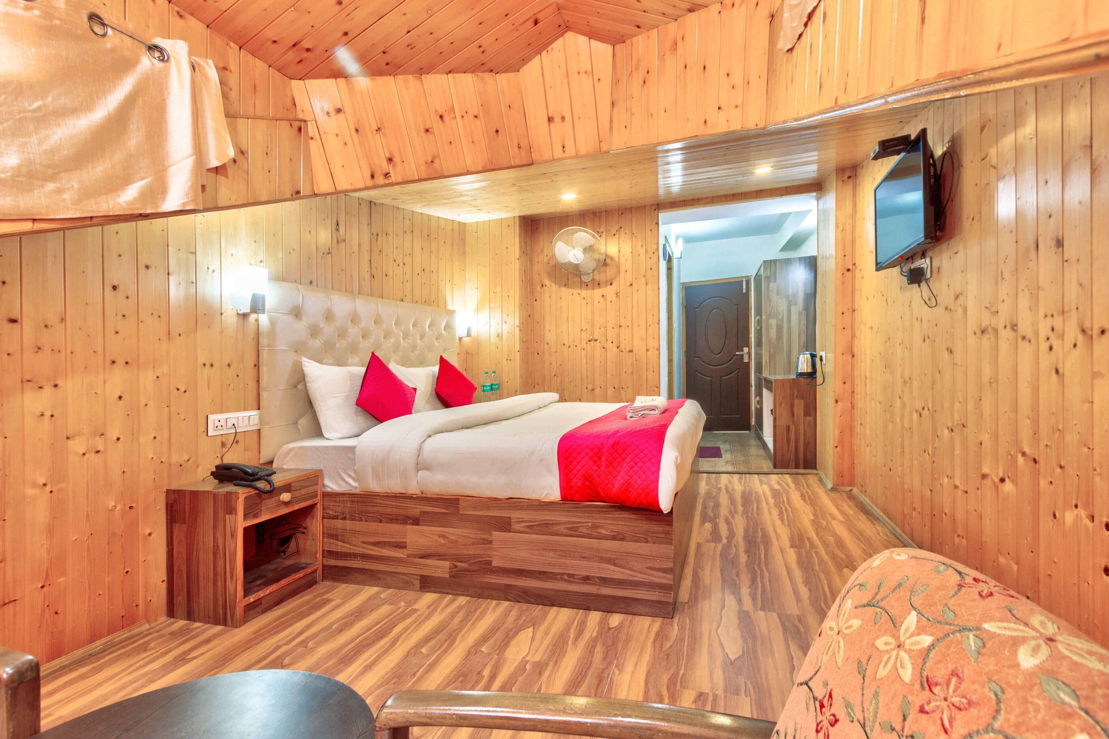 Een slaapkamer met houten inrichting, een bed, nachtkastje en een aan de muur bevestigde televisie.
