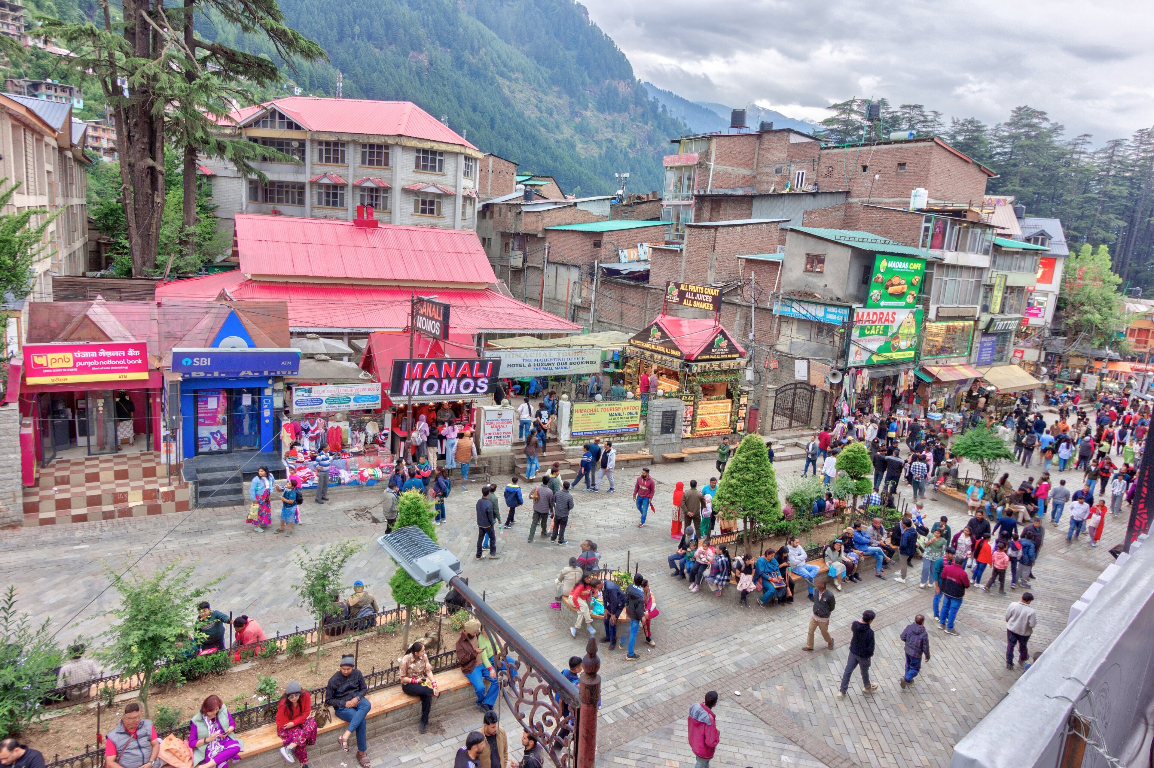 A bustling street scene with various shops and buildings, including a prominent sign for 'Manali Homos'.