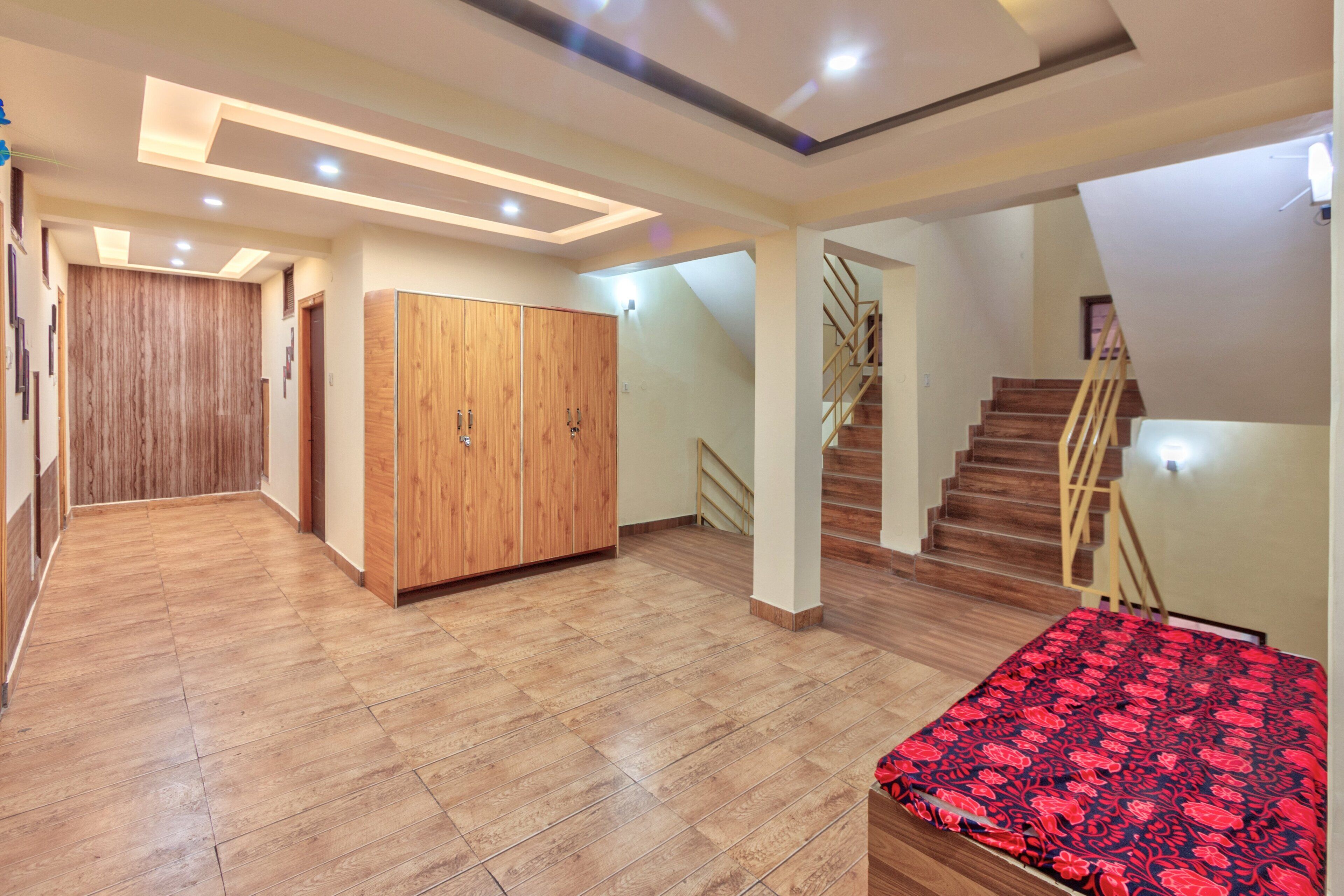 A spacious room with a wooden floor, a large wardrobe, a staircase, and a bed with a patterned bedspread.