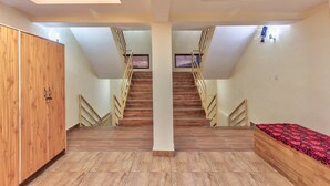 A room with a wooden wardrobe, a bed with a red patterned bedspread, a wooden staircase, and a ceiling with recessed lighting. - The mount Heaven Hotel  Vijayant (Manali)