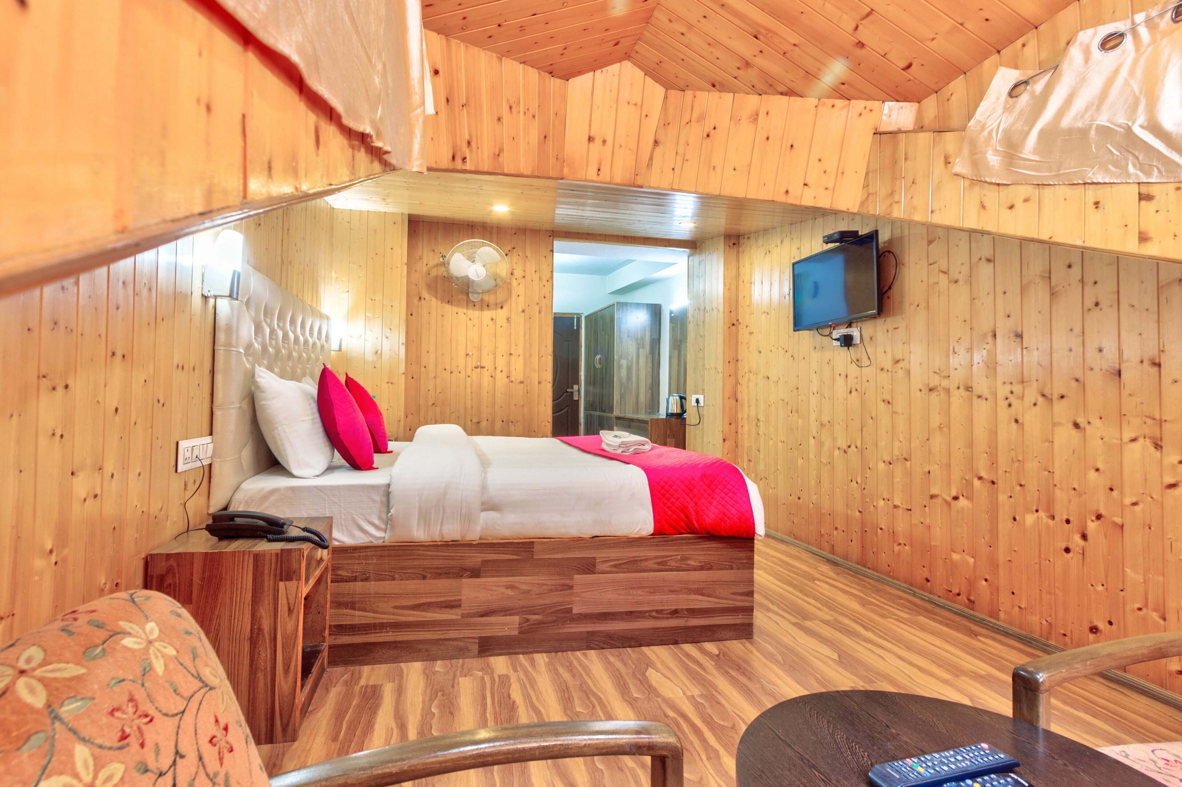 A wooden-paneled room with a bed, a TV mounted on the wall, and a small table with a chair.