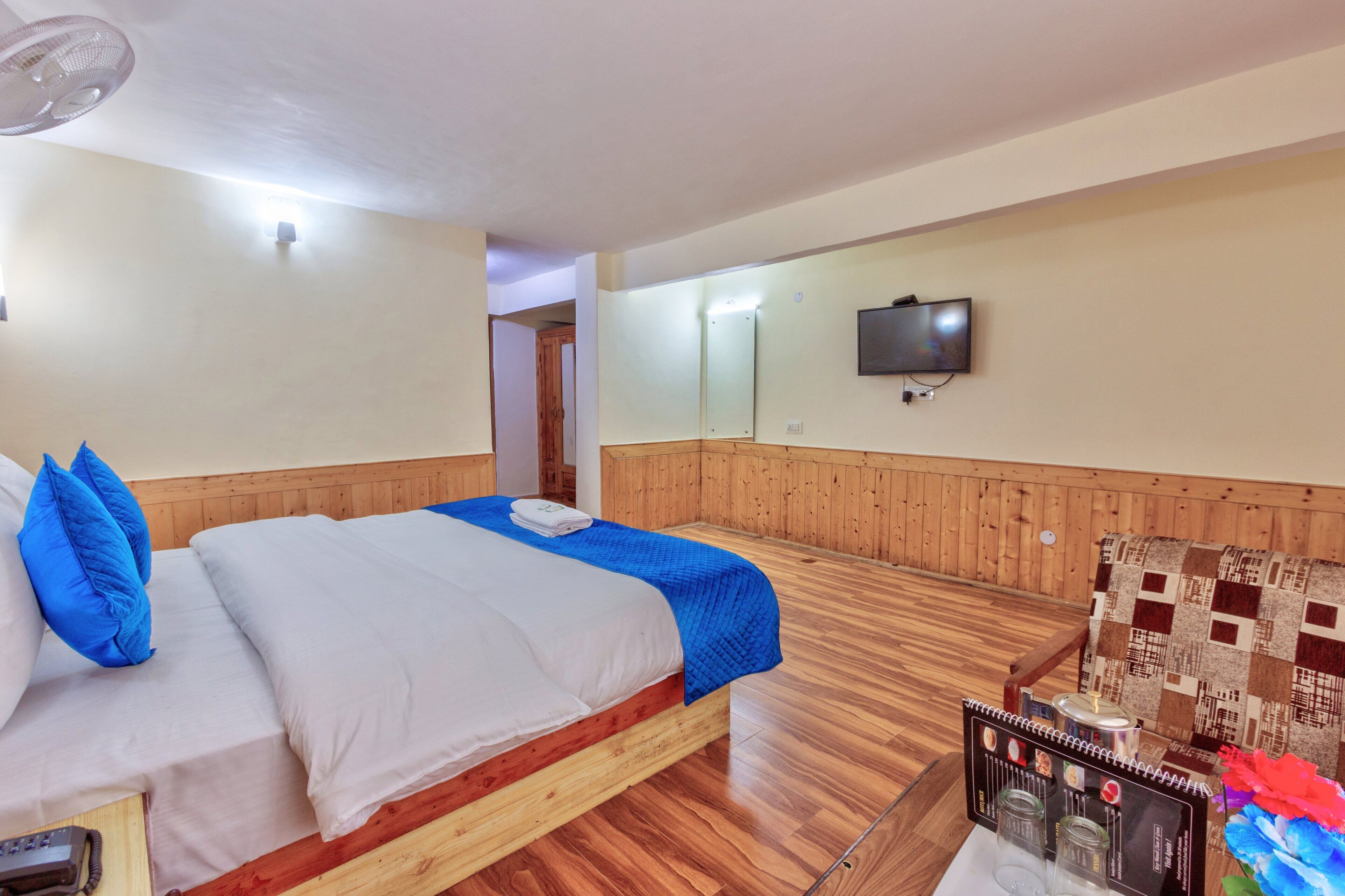 Une chambre d’hôtel avec un lit en bois, un téléviseur fixé au mur et une petite table avec un menu.