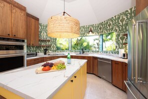 Une cuisine moderne dotée d’un îlot central, de meubles en bois, d’un réfrigérateur en acier inoxydable et d’une grande fenêtre offrant une vue sur la verdure.