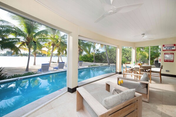 Un espace aménagé au bord de la piscine, avec vue sur la plage, comprenant des chaises longues et une table à manger.
