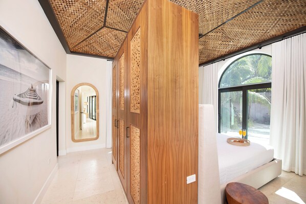 Una habitación de hotel moderna con un ventanal grande, una cama, un armario de madera y un espejo.