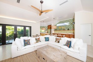 Un salon spacieux avec un canapé d’angle blanc, une table basse en bois et un ventilateur de plafond.
