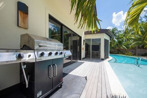 Un barbecue extérieur doté d’une porte coulissante en verre donnant accès à une zone avec piscine.