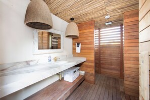 A bathroom with wooden slats, a marble sink, and a shower with a wooden door. - Kai Cove: Stunning Bali Beach House w/ Pool + Dock on Bio Bay (Cayman Kai)