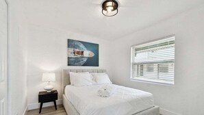 Una camera da letto con un letto, un comodino, una lampada, un quadro raffigurante una barca e una finestra con persiane.