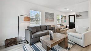 Un soggiorno moderno con un divano modulare grigio, un tavolino in legno e una poltrona bianca. Si nota una lampada da terra e un quadro appeso al muro.