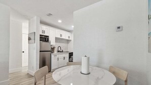 Una cocina moderna con armarios blancos, electrodomésticos de acero inoxidable y una mesa de comedor de mármol con sillas.
