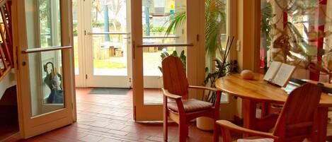 An open door leading to a patio with a dining table and chairs, a bookshelf, and a glass door reflecting the outside.