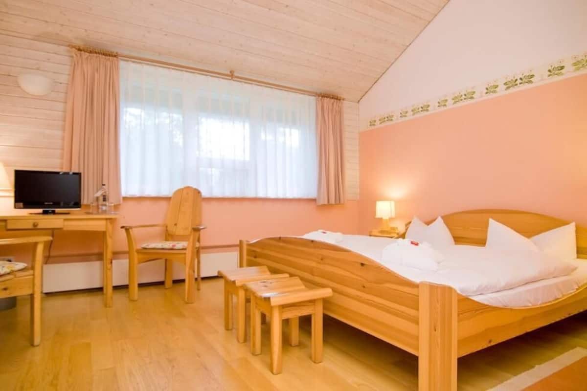 Un lit en bois avec une literie blanche, un bureau avec un ordinateur, une chaise et une petite table.