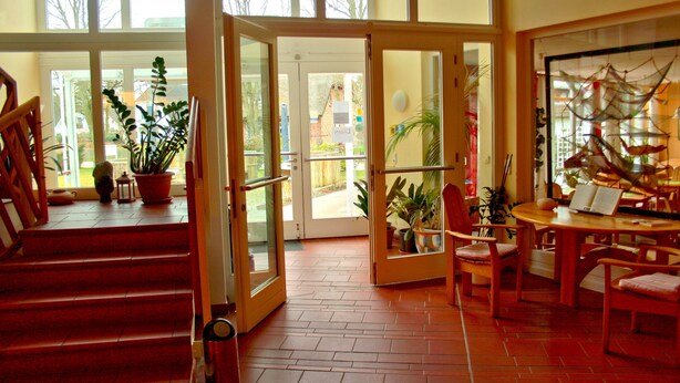 A hotel lobby with a staircase, a reception desk, and potted plants. - Hotel Haus Linden (Ostseebad Prerow)