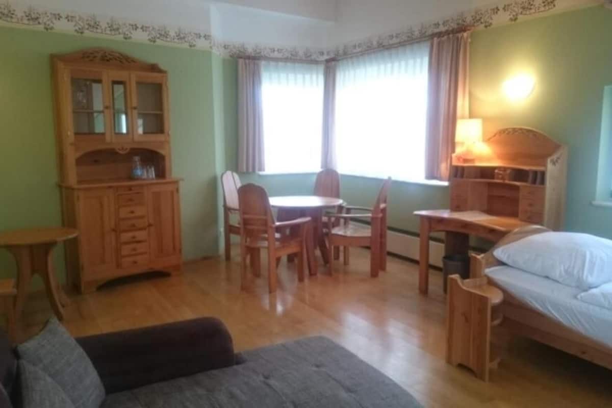 Une pièce comprenant un lit, une armoire en bois, une table à manger avec des chaises et une petite table d’appoint.