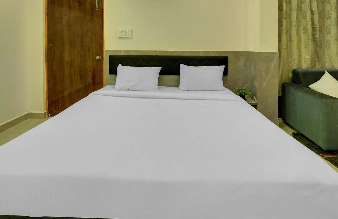 A neatly made bed with white sheets and pillows, a dark headboard, a green armchair, and a wooden door.