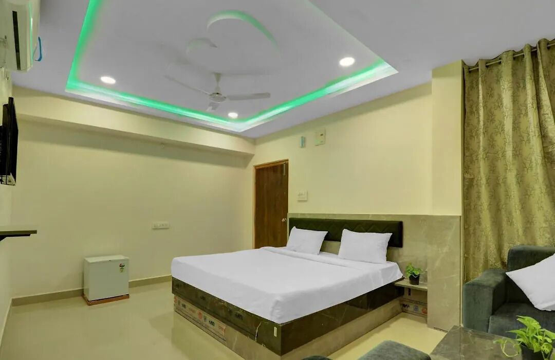 A hotel room with a bed, a ceiling fan, a small table, a chair, and a potted plant.
