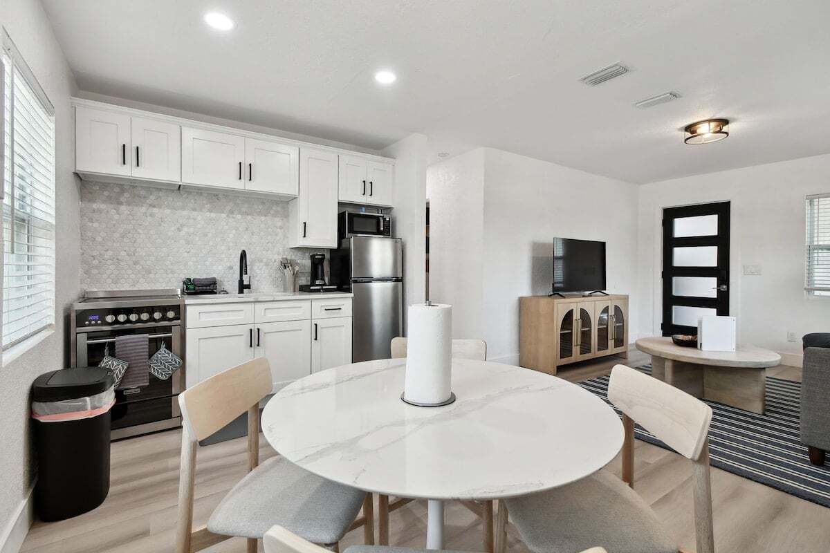 A modern kitchen with white cabinets, a stainless steel refrigerator, and a microwave. There is a round dining table with chairs.