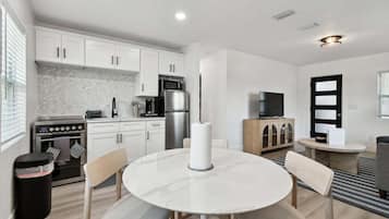 A modern kitchen with white cabinets, a stainless steel refrigerator, and a microwave. There is a round dining table with chairs.