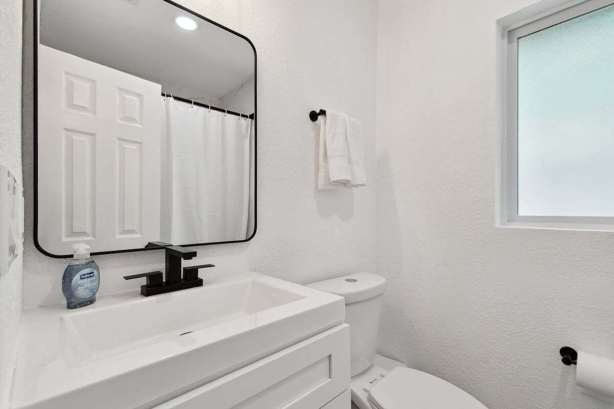 A bathroom with a white sink, a mirror, a toilet, and a window.