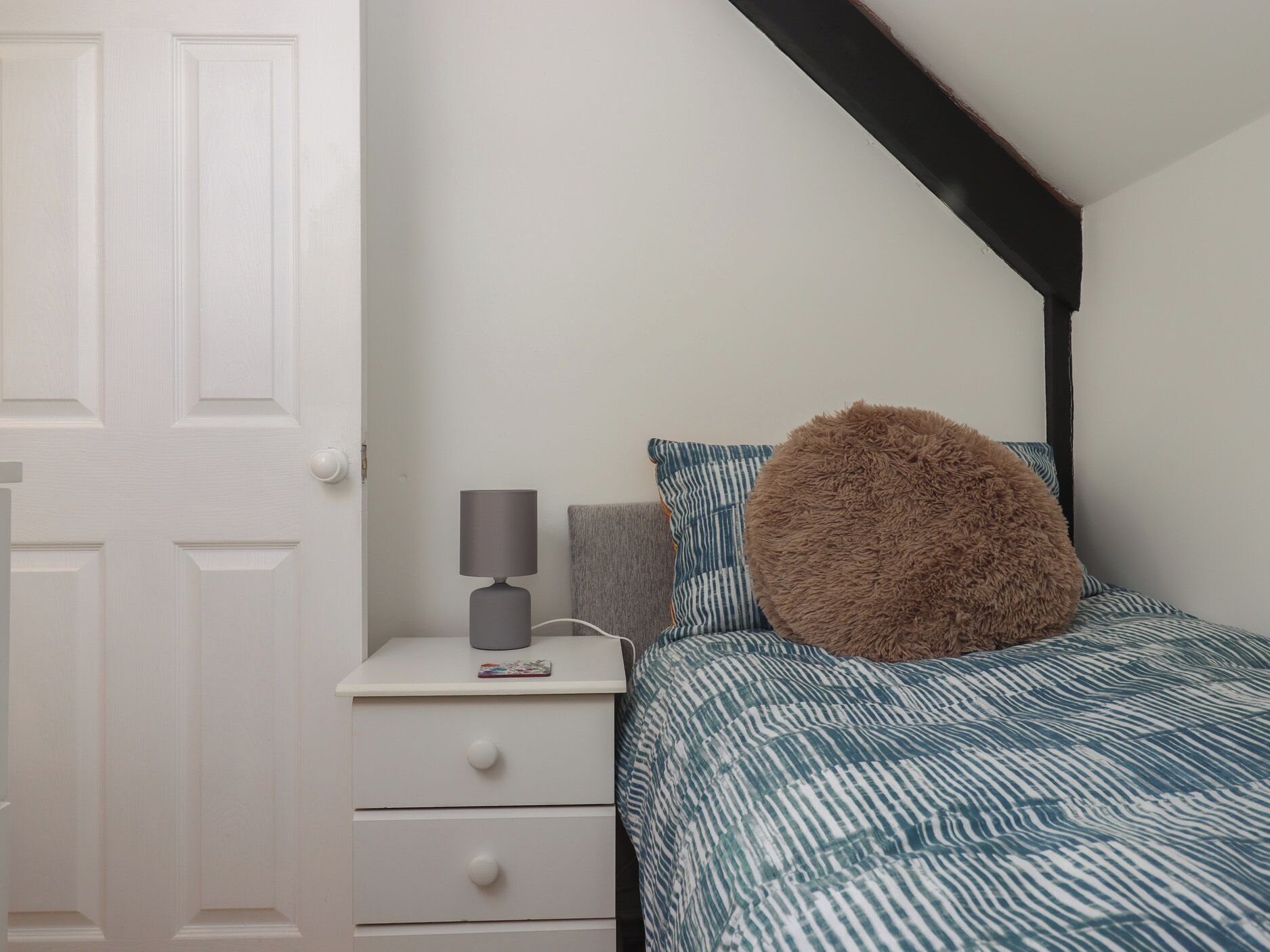 A bedroom with a bed, a nightstand, a lamp, and a door.