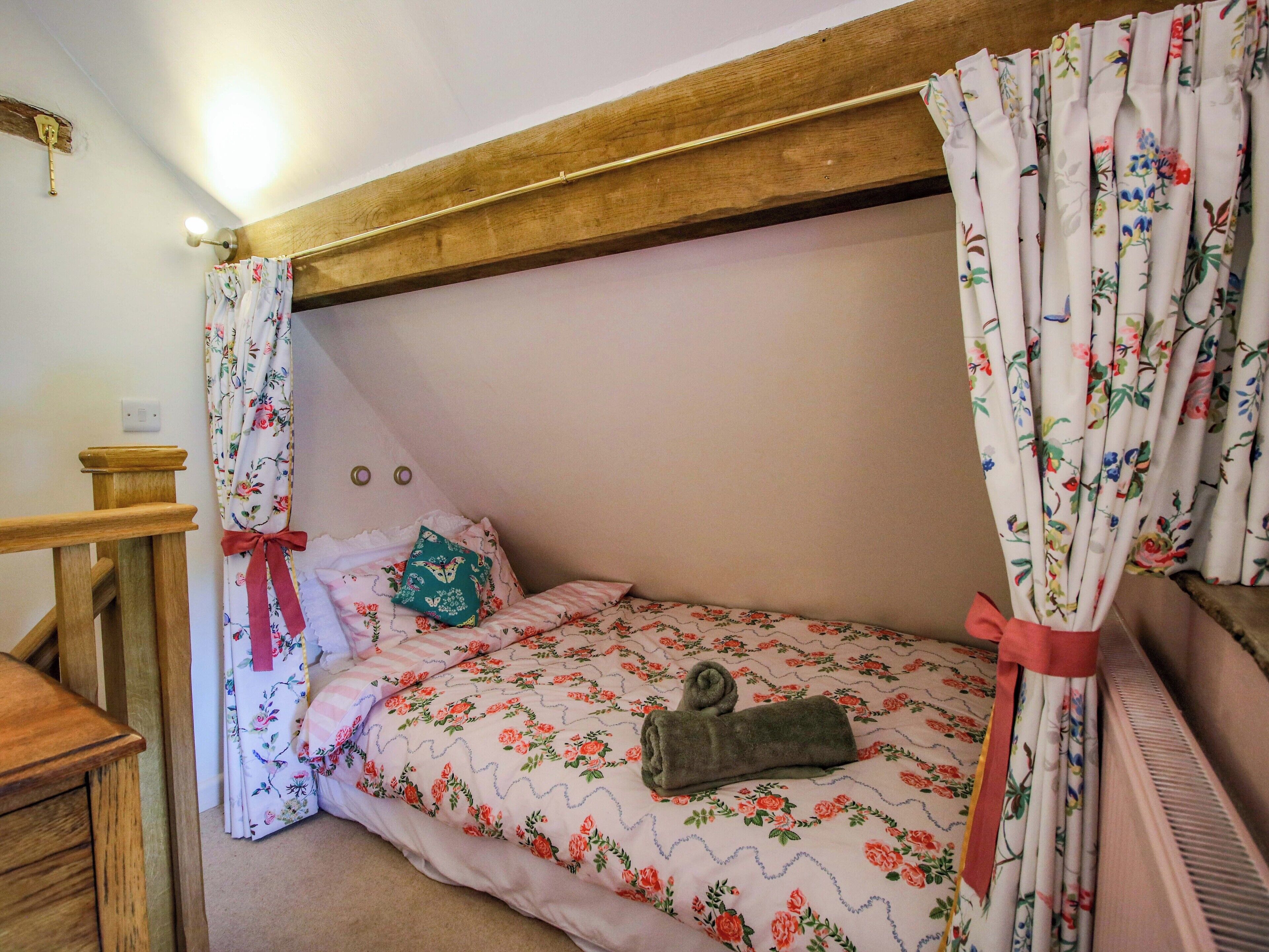 A small, cozy bedroom with a wooden ceiling, floral bedding, and a single bed with a rolled towel.