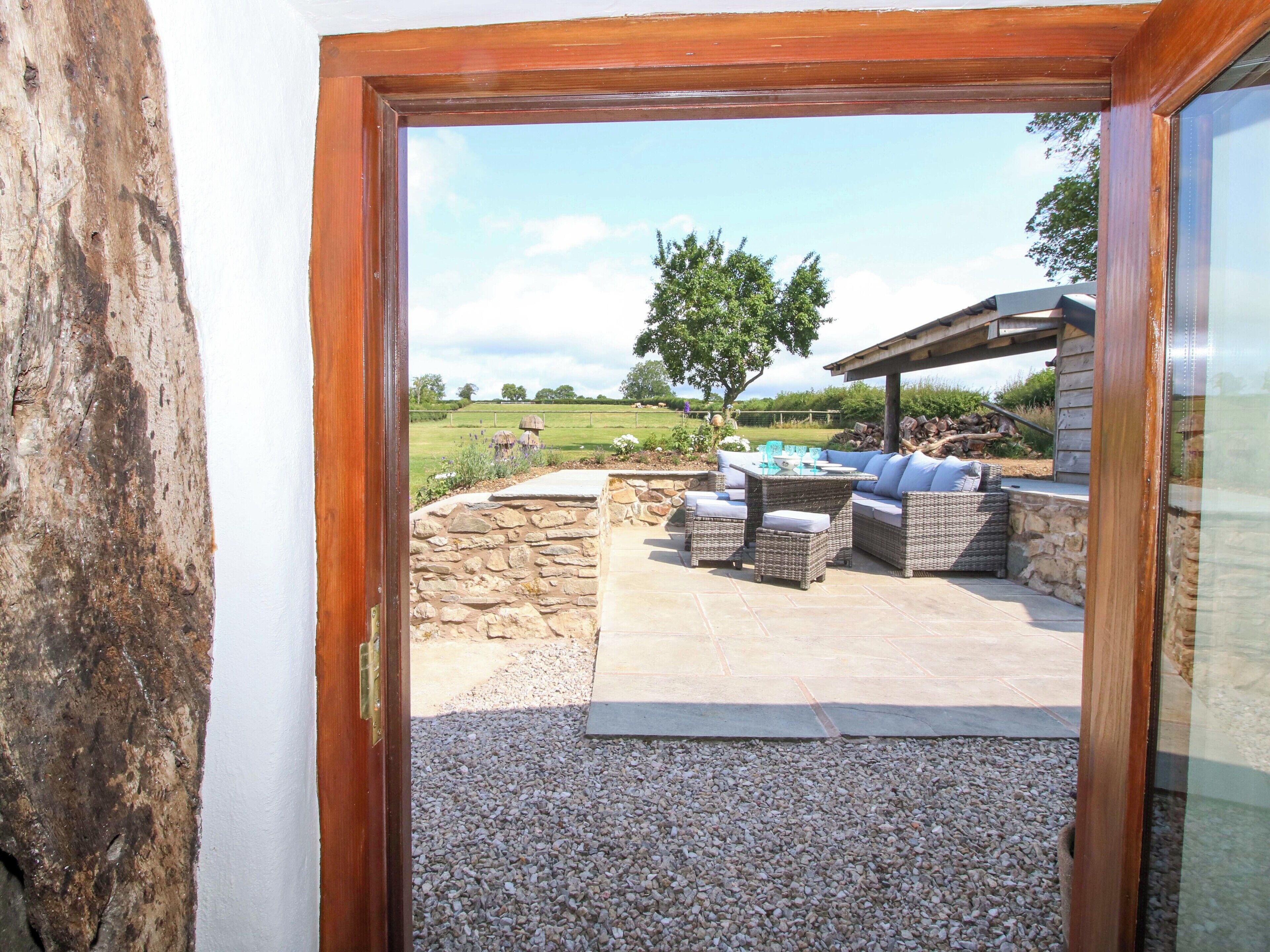 An outdoor patio area with stone walls, a seating arrangement, and a view of a grassy field and trees.