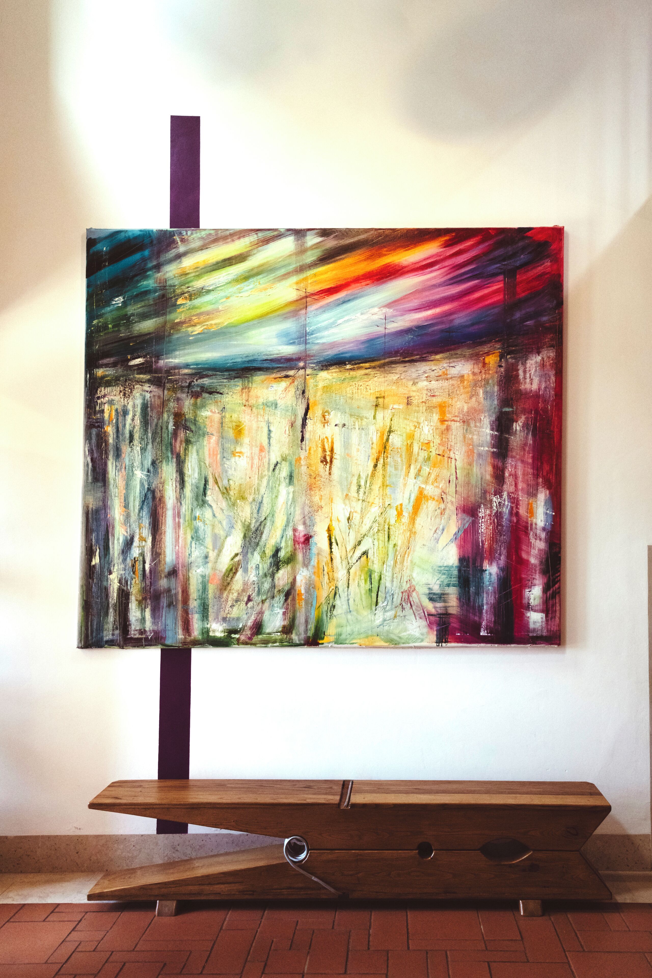 Un grande quadro astratto appeso al muro, di fronte a una panca in legno.