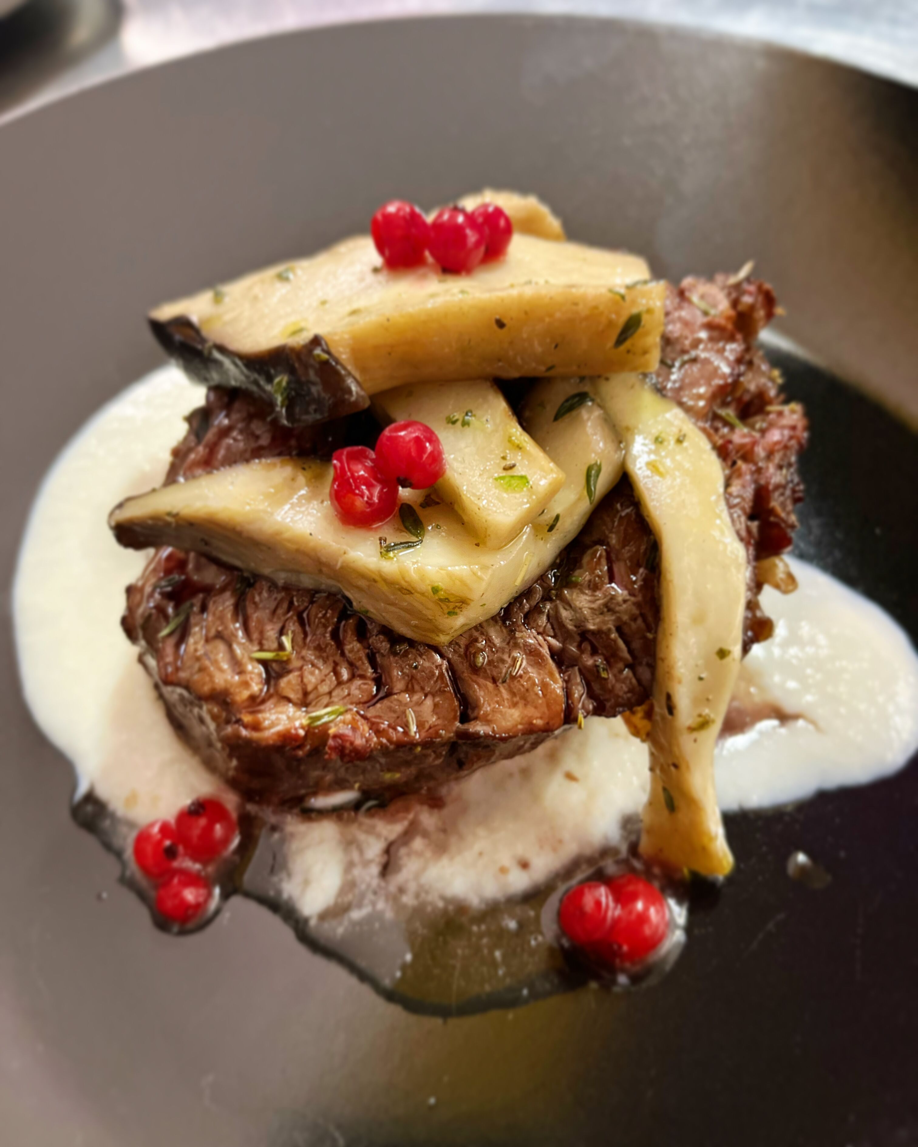A steak with mushrooms and red berries on a plate.