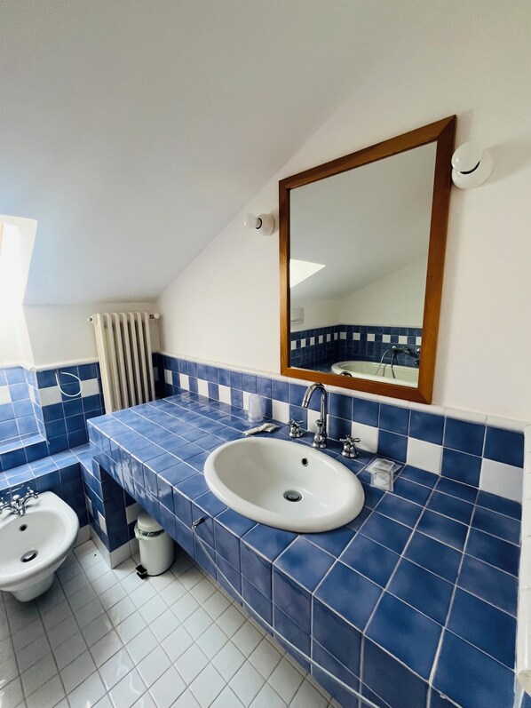 Un baño con lavamanos blanco, azulejos azules, espejo con marco de madera y radiador blanco.