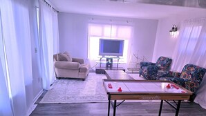 Ein Wohnzimmer mit einer Couch, einem Sessel und einem Tisch mit zwei Fernbedienungen.