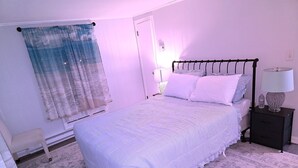 Ein Schlafzimmer mit Bett, Nachttisch, Lampe und einem Fenster mit Vorhängen.