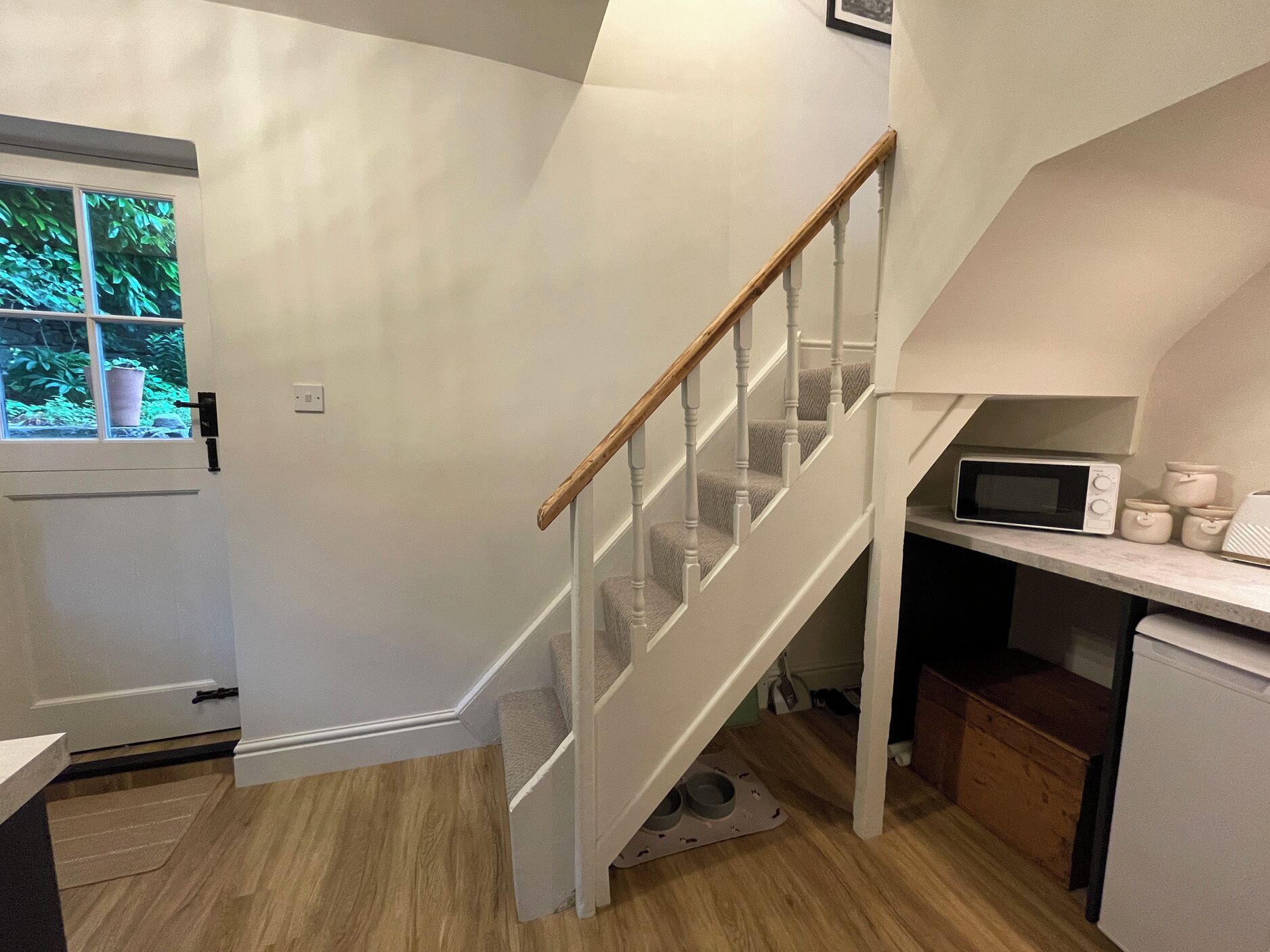 A kitchen with a microwave, cabinets, and a wooden staircase.