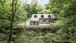 Una casa de piedra con patio vallado, rodeada de un bosque denso.