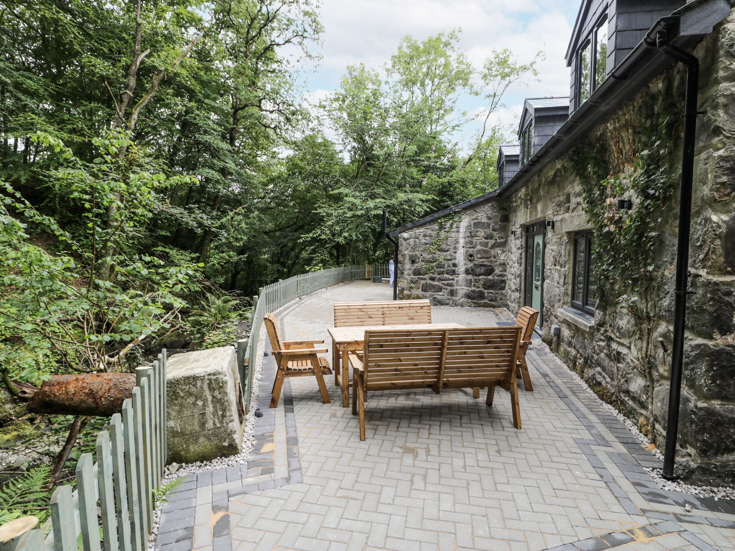 A patio with a table and chairs, surrounded by stone walls and greenery.