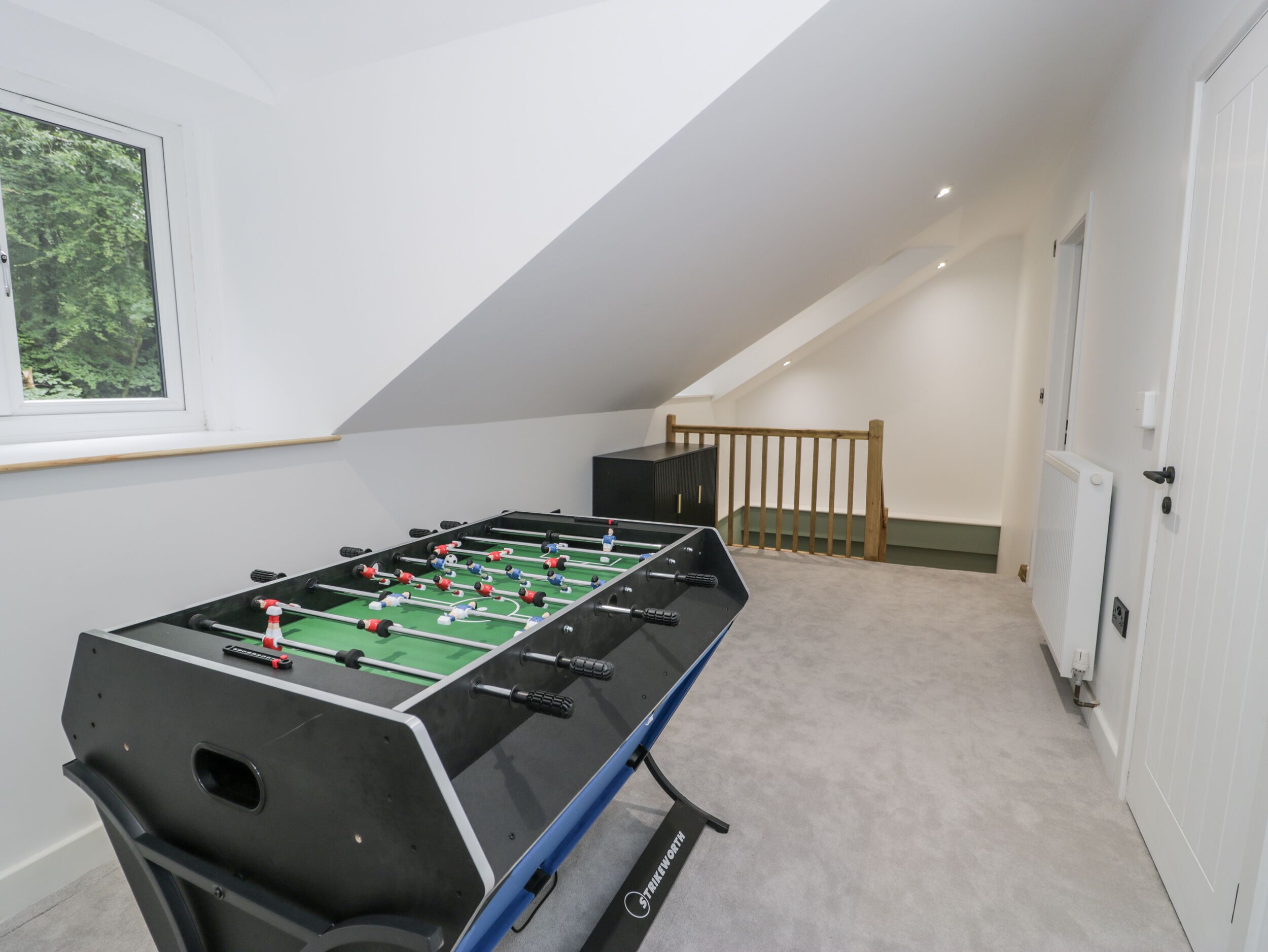 A foosball table in a room with a sloped ceiling, a window, and a door.