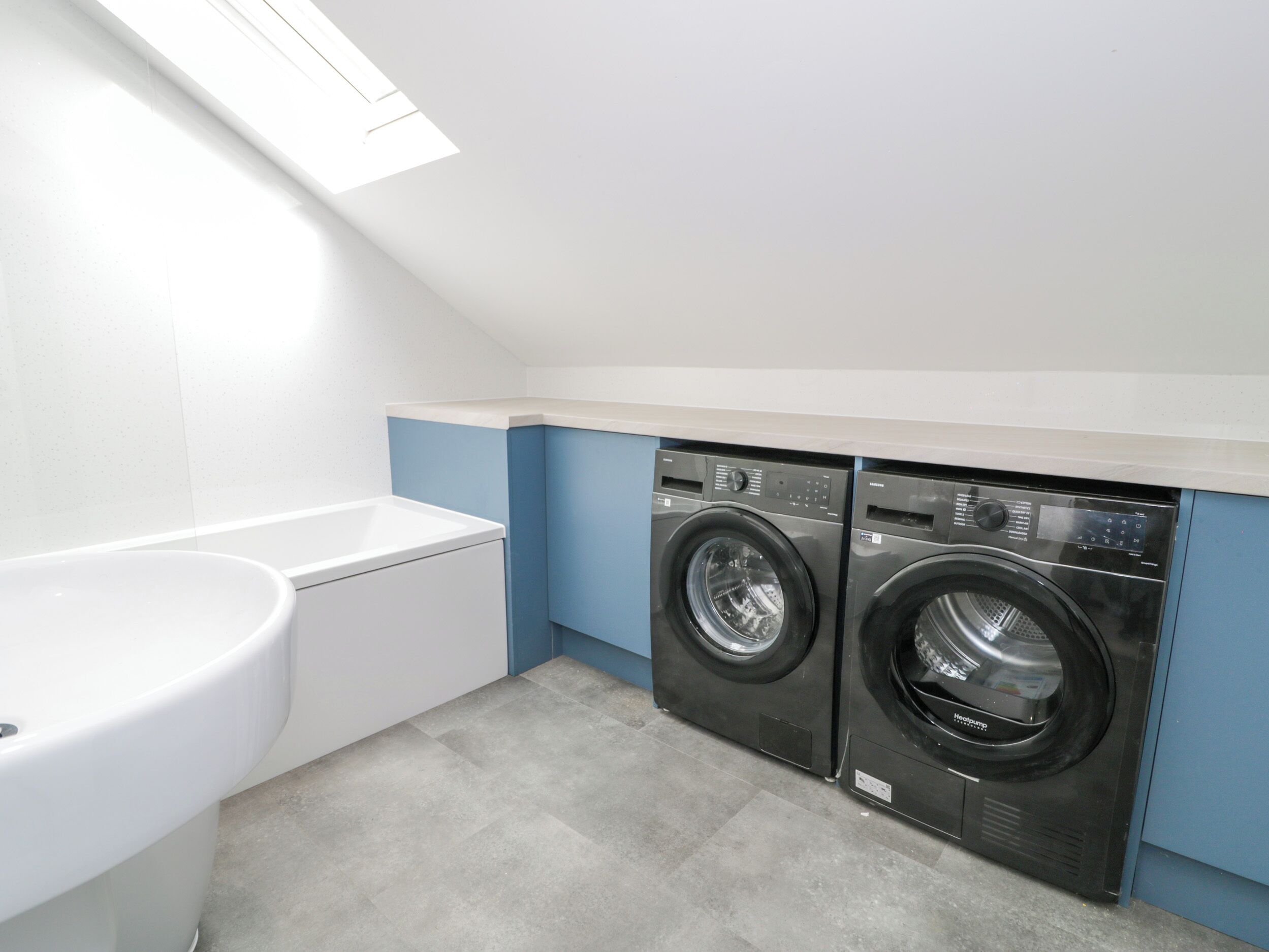 A laundry room with two front-loading washing machines, a white sink, and a skylight above.