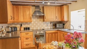 Cucina con mobili in legno, cappa in acciaio inossidabile, microonde e lavello. Un tavolo da pranzo con un vaso di fiori e un piatto di cibo.