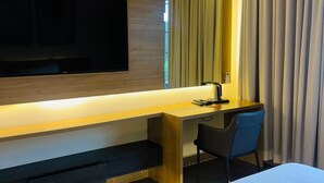 A hotel room with a bed, a desk with a chair, a flat-screen TV mounted on the wall, and an air conditioning unit. - CMG Hotels Ltd (Tarime)