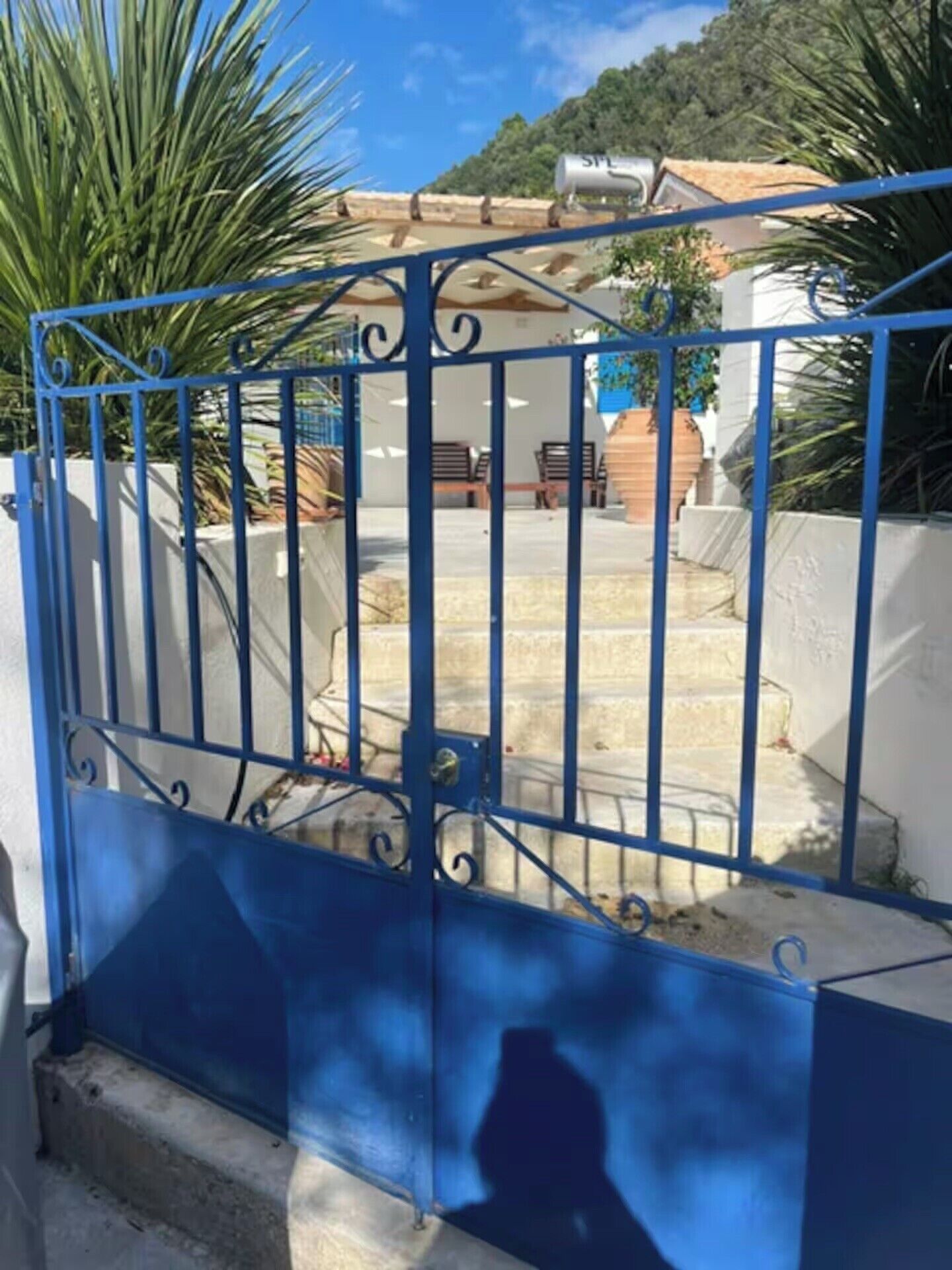 A blue metal gate with a spiral design, leading to a staircase with a white wall and a tiled roof.