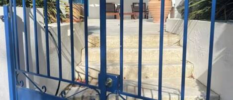 A blue metal gate with a spiral design, leading to a staircase with a white wall and a tiled roof.