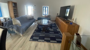 Una sala de estar con un sofá, una mesa de centro de vidrio, un televisor y un mueble de madera.