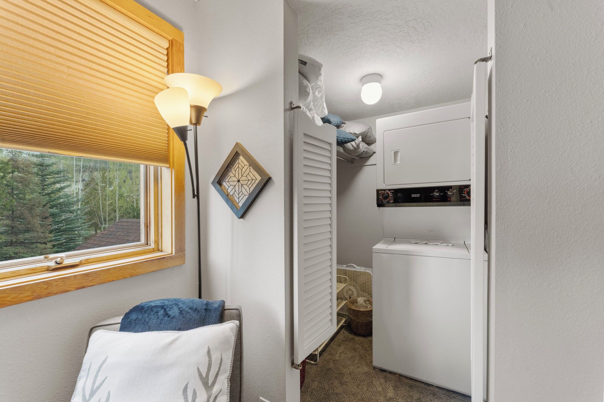 Une chambre à coucher de taille modeste, dotée d’une fenêtre, d’un radiateur, d’une machine à laver et d’un luminaire au plafond.