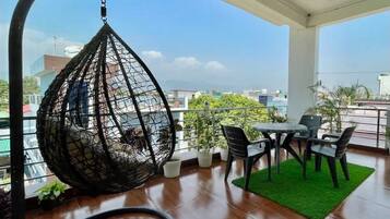 Enjoy the city view from this balcony with a hanging chair, table, and potted plants.