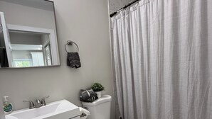 A modern bathroom with a white sink, mirror, and toilet. There is a shower curtain, a small potted plant, and a towel rack.