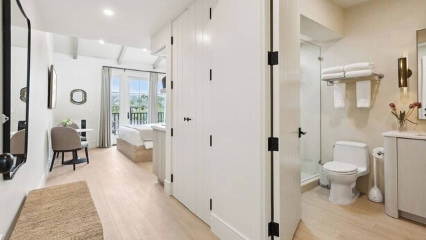 A modern hotel room with a bed, a desk, a chair, and a bathroom with a toilet and sink. - Casa Riviera 21 - Boutique Suites (Santa Barbara)